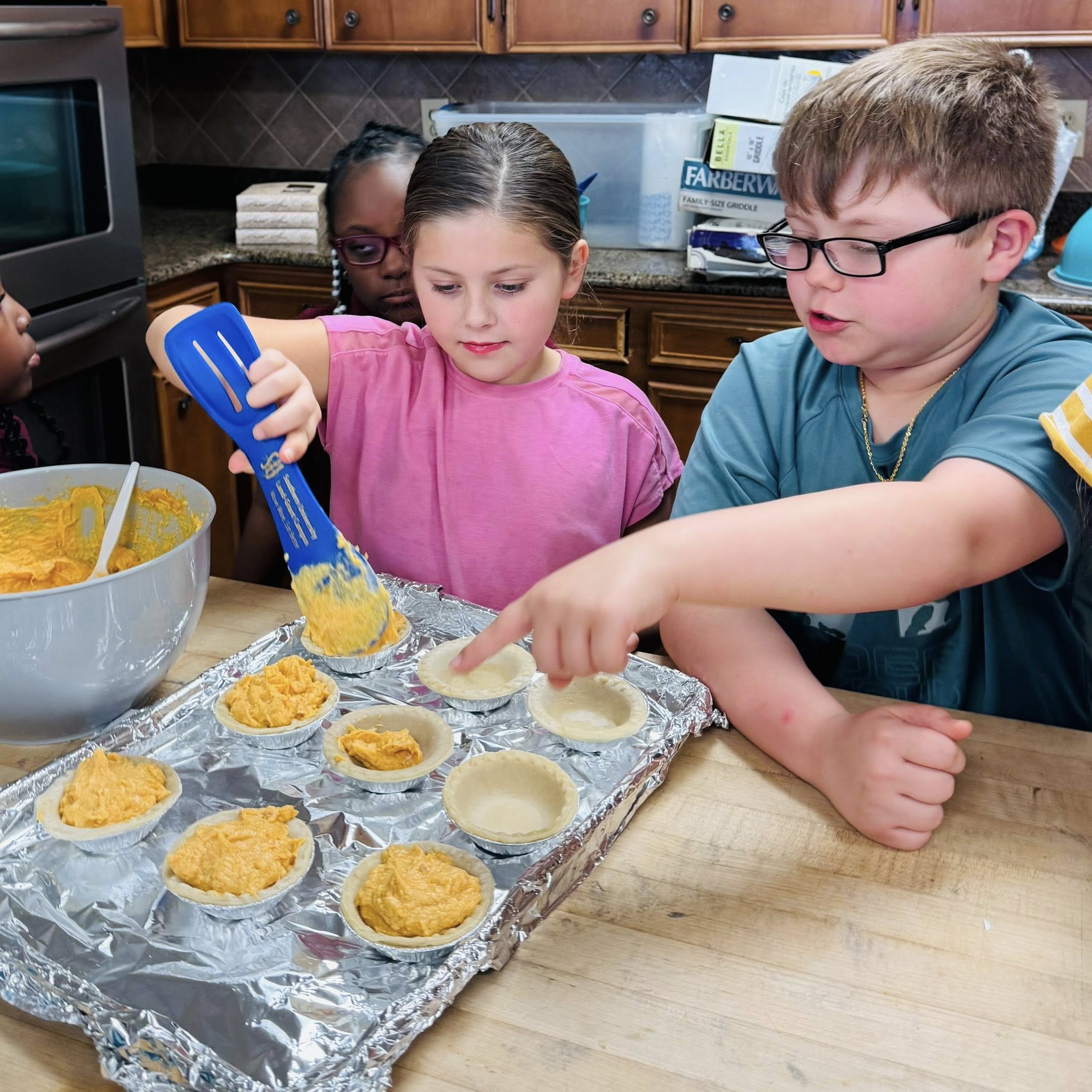 A boy watching a girl put pie filling into mini pie shells.